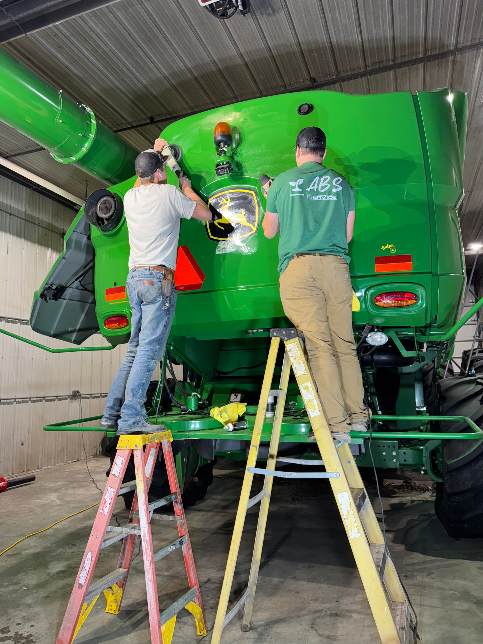 Two technicians polishing a green combine in a large shop