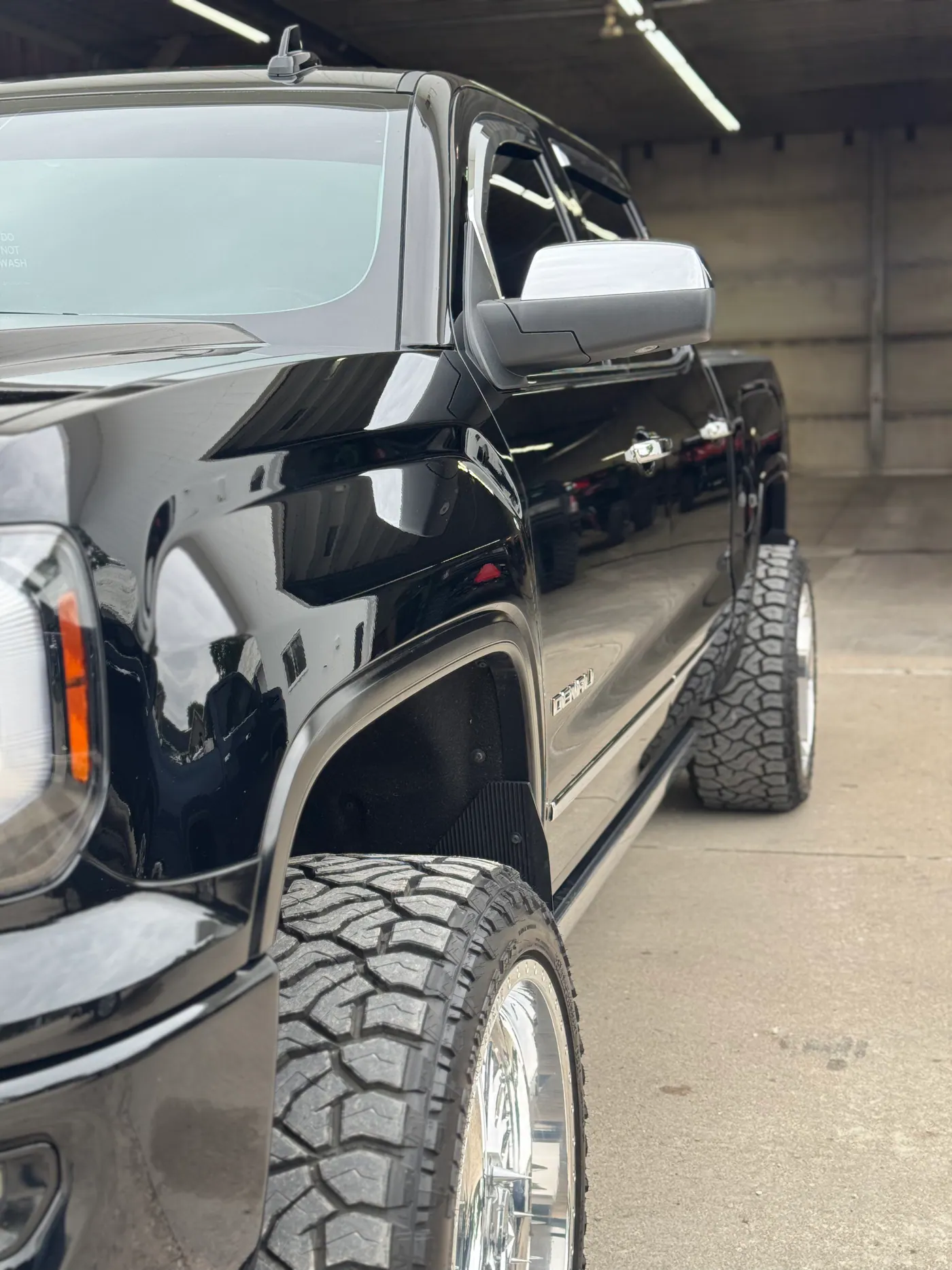 Glossy black GMC pickup viewed along the driver side in a shop