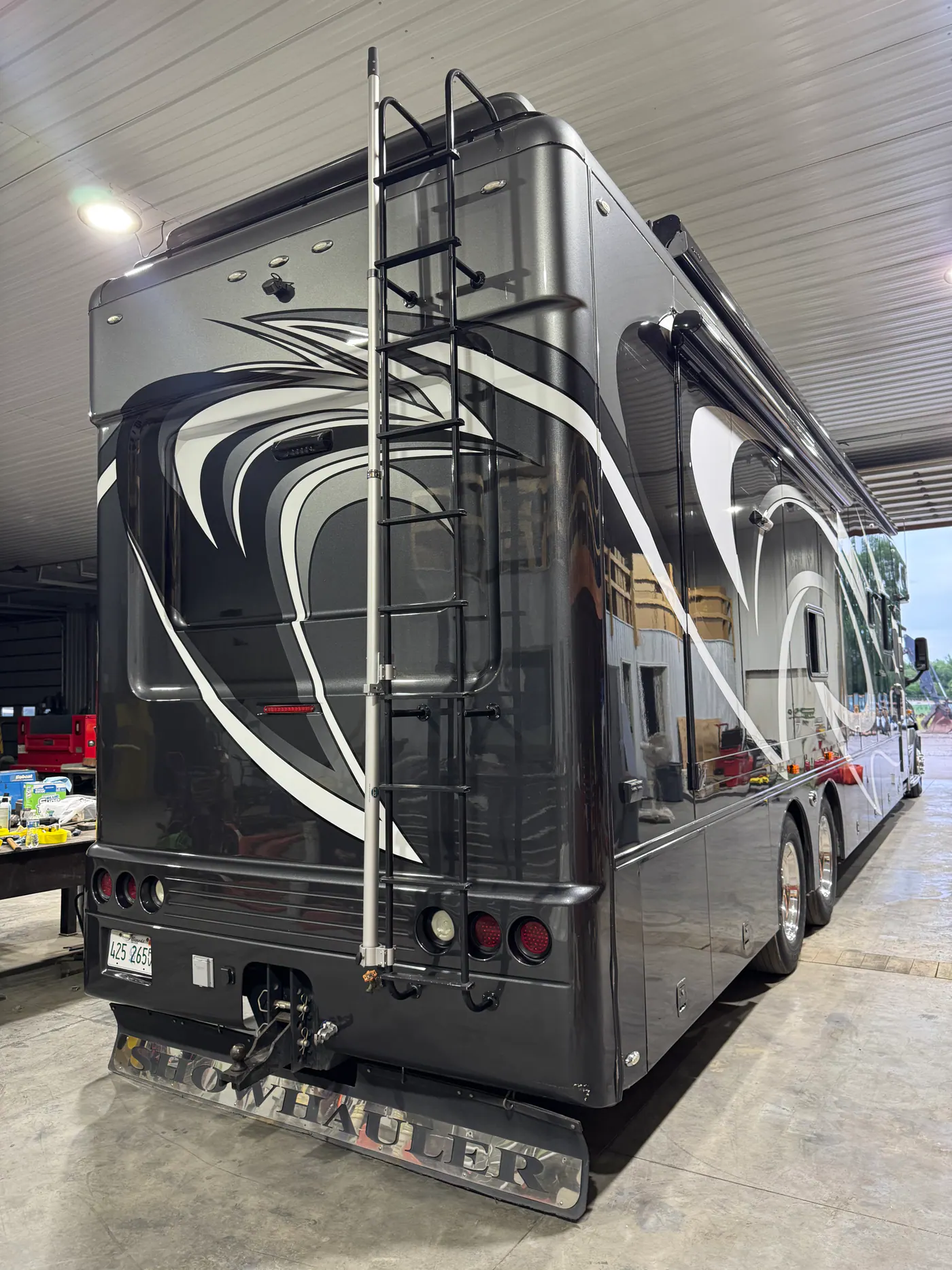 Rear view of a black, gray, and white motorhome inside a shop