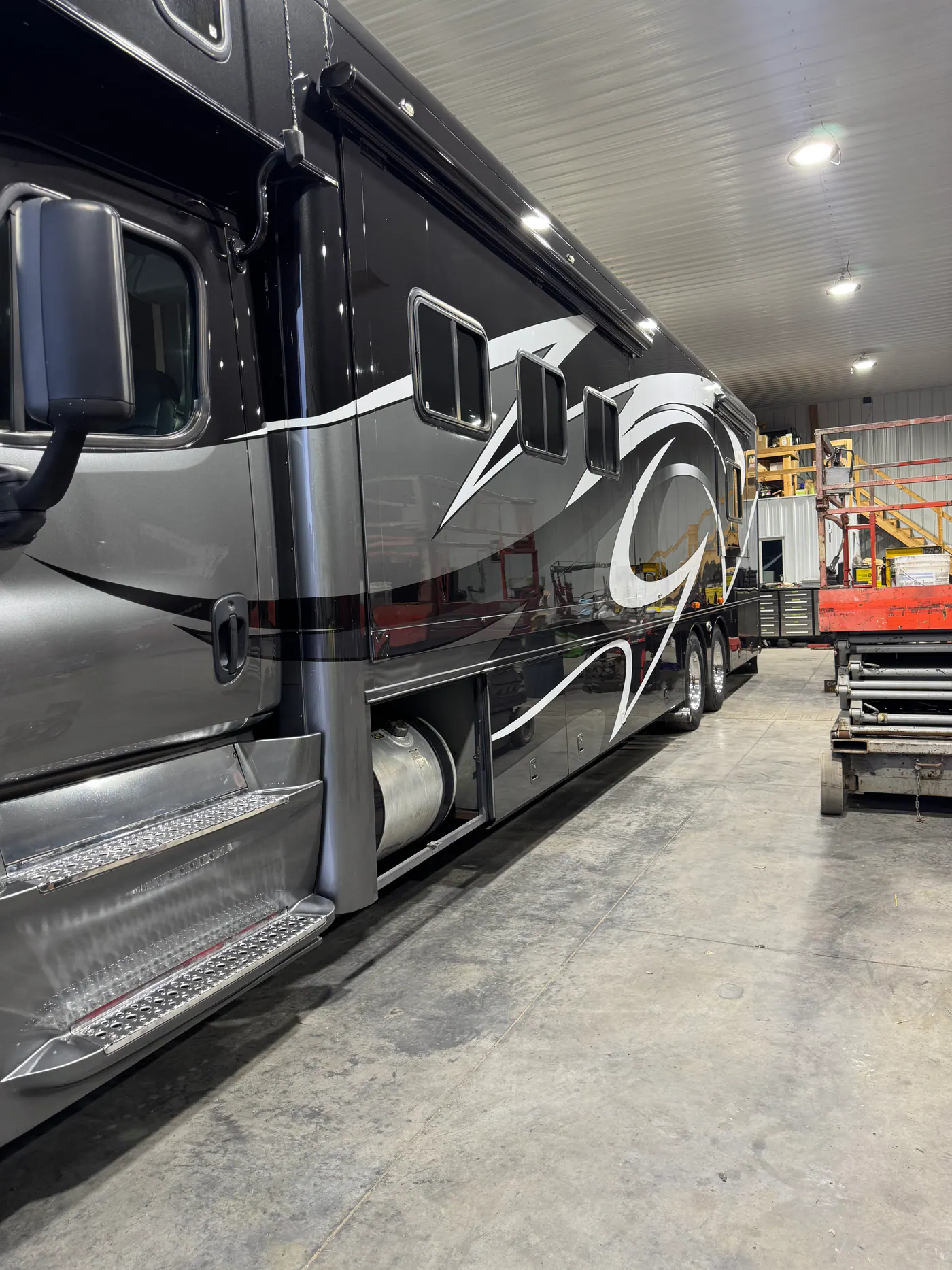 Long side view of a black and gray motorhome inside a shop