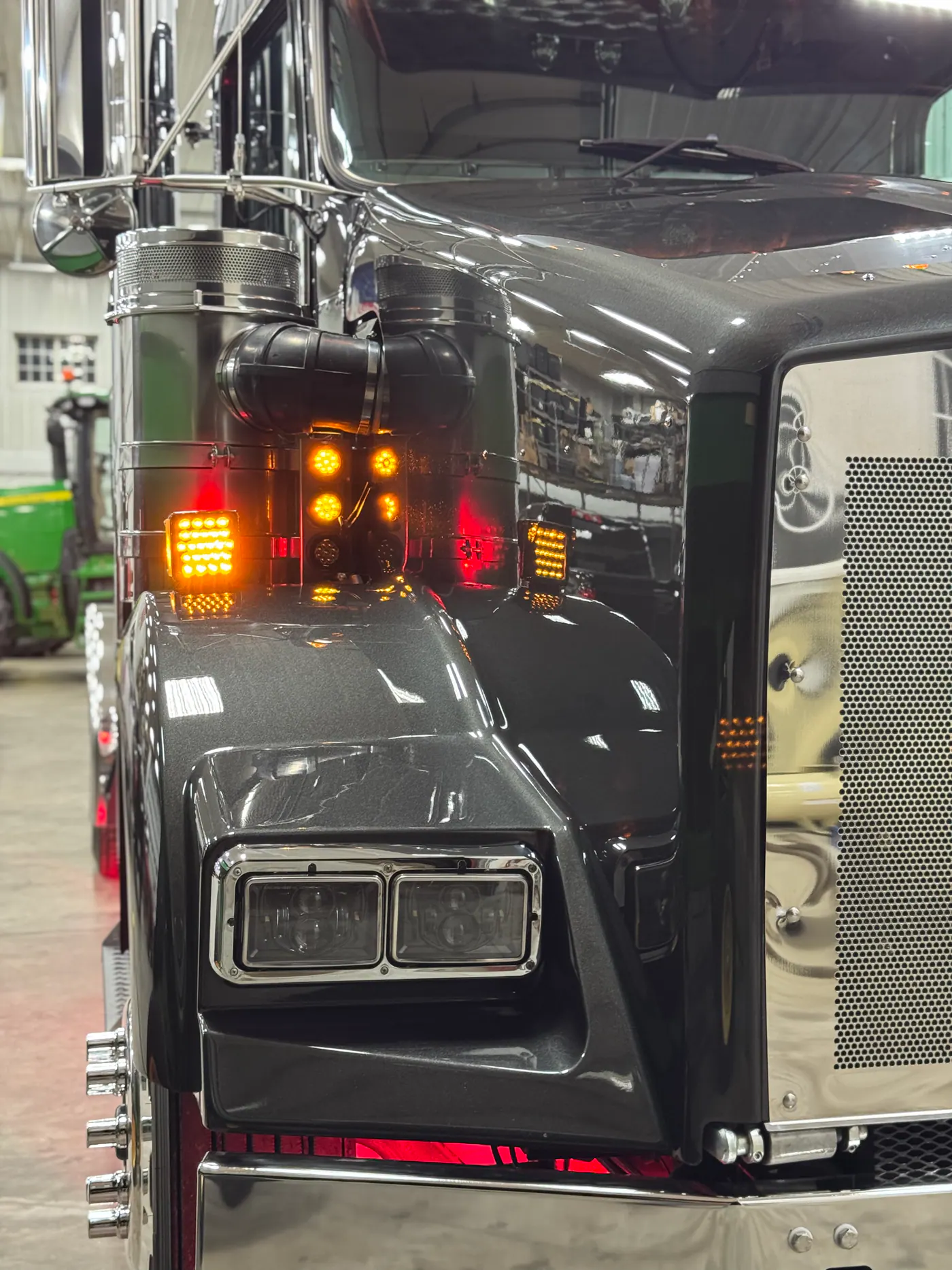 Close view of a black semi truck headlight and chrome grille