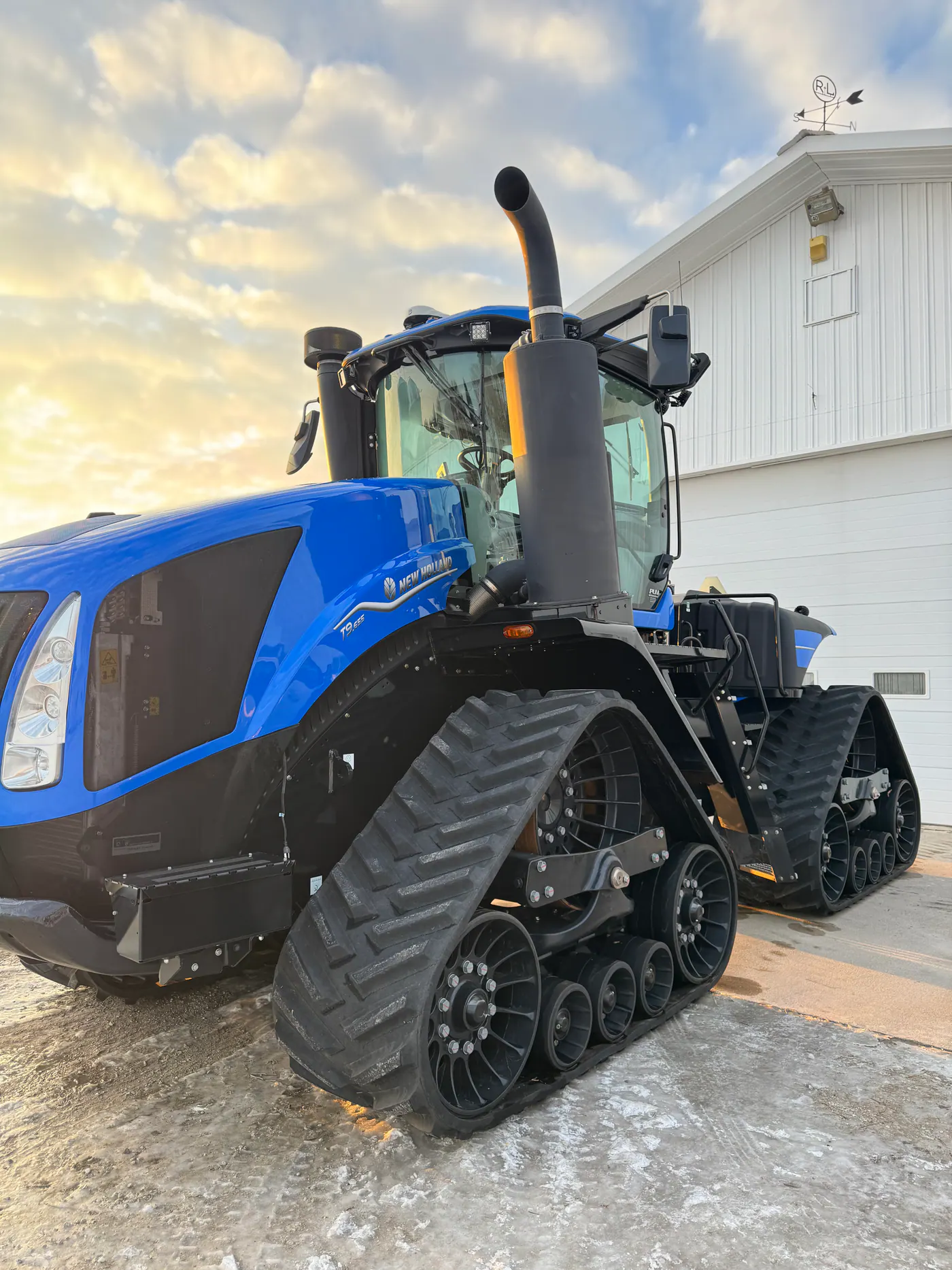 Blue New Holland tracked tractor parked outside a white building