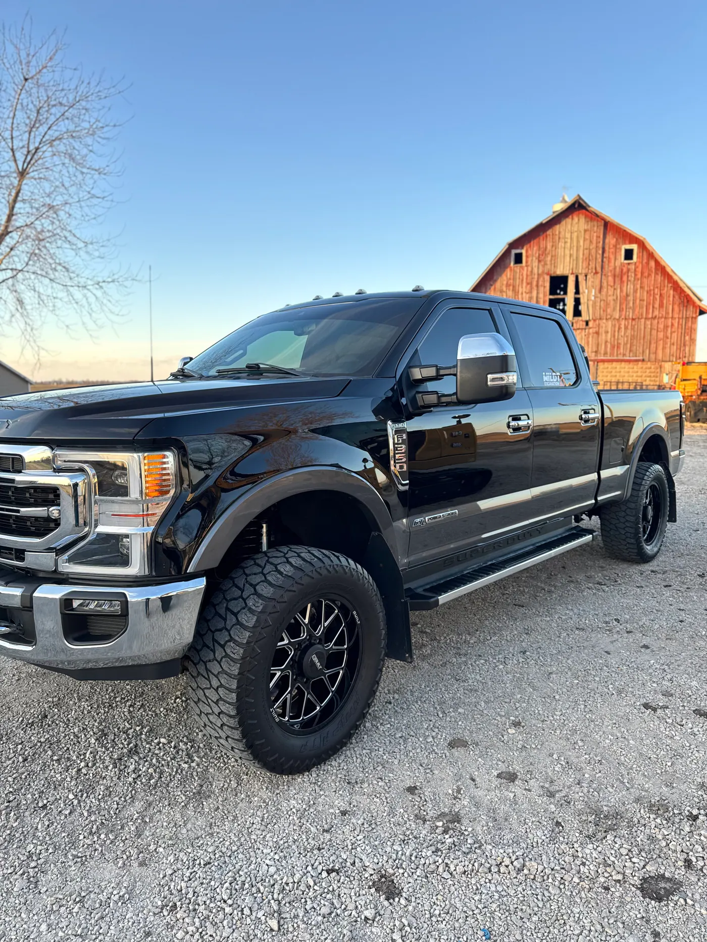 Black Ford Super Duty pickup parked in front of a red barn