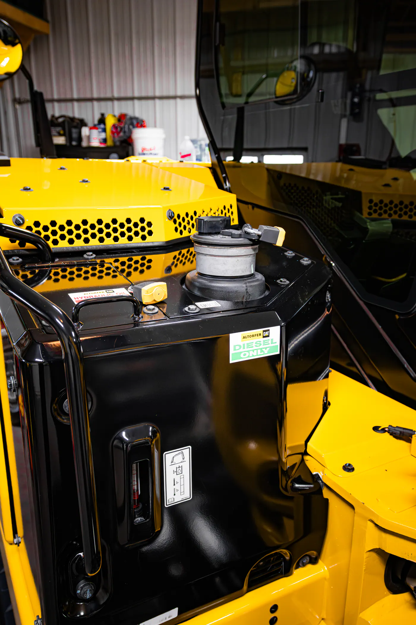 Yellow excavator fuel tank and cab detail inside a shop