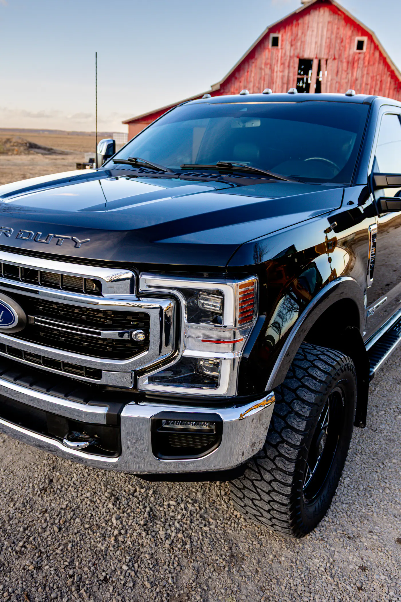 Black Ford Super Duty pickup photographed beside a red barn