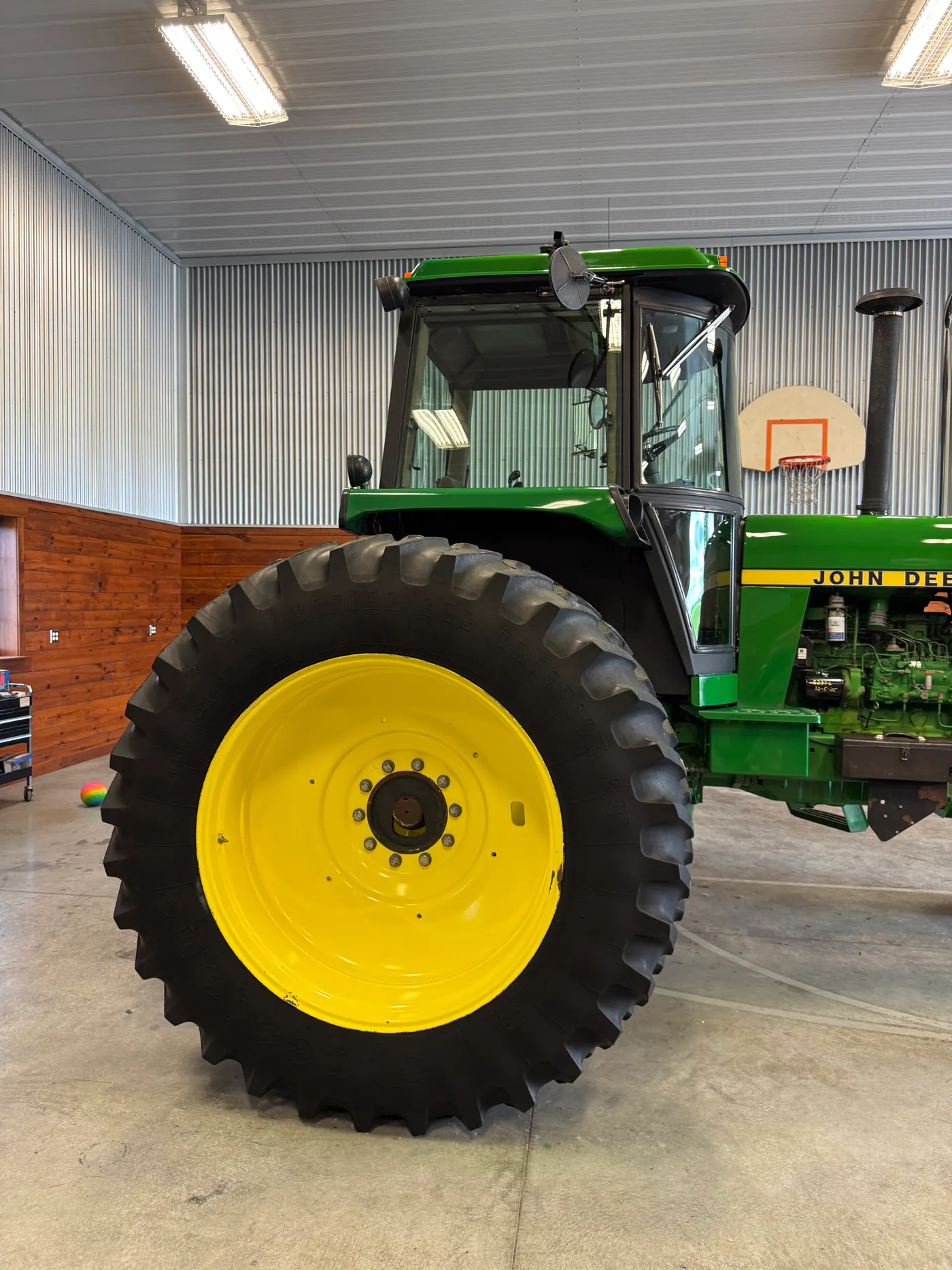 Green John Deere tractor with large yellow rear wheel in a shop