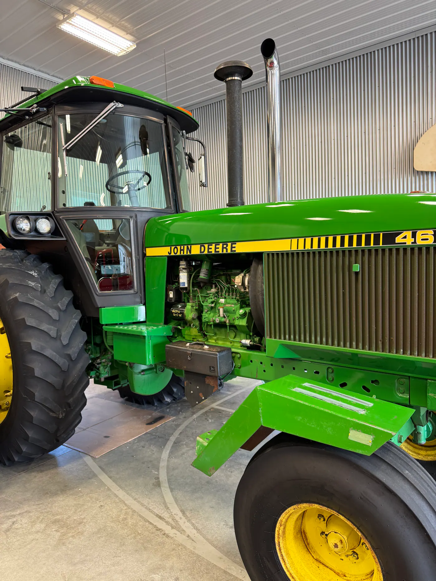 Green John Deere tractor photographed from the side indoors