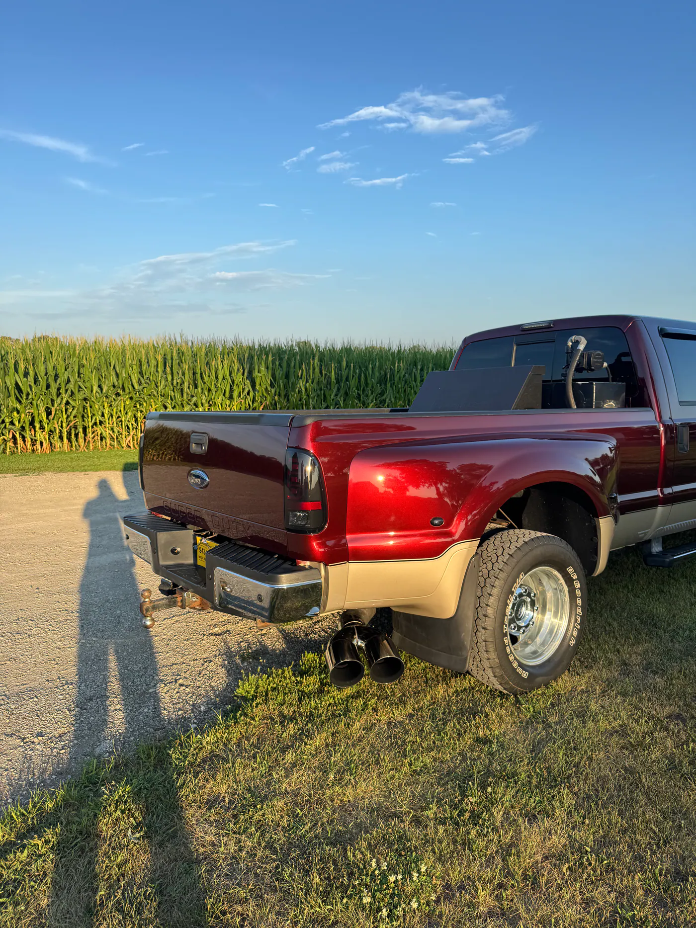 Rear quarter of a burgundy Ford dually pickup beside a cornfield