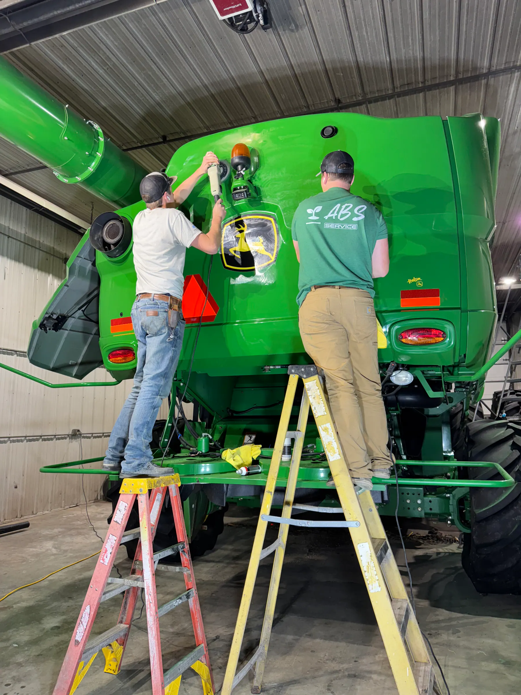 Premier Coatings team polishing the green finish of agricultural equipment in a large shop