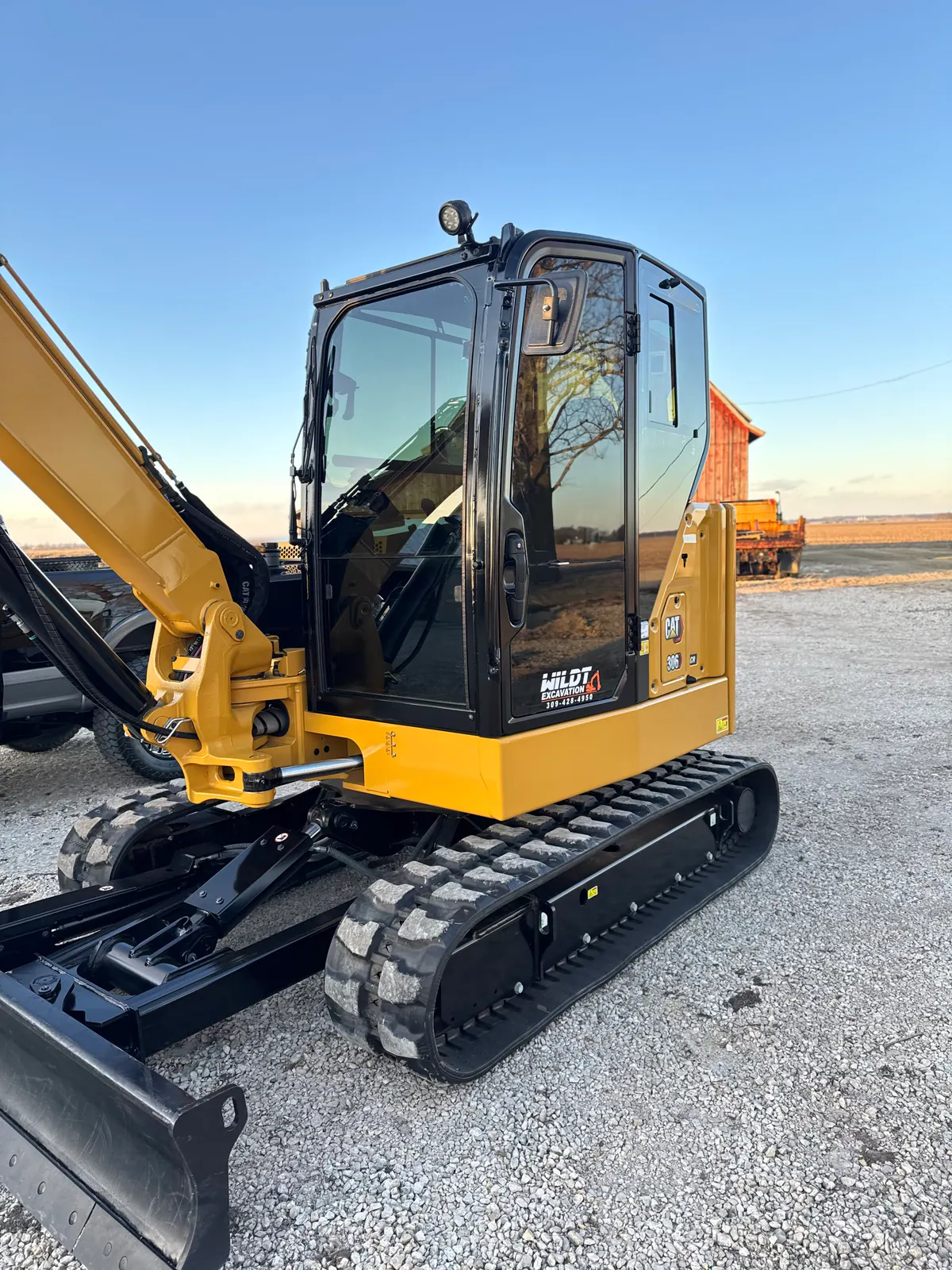 Clean yellow excavator with black cab and tracks outside a farm shop